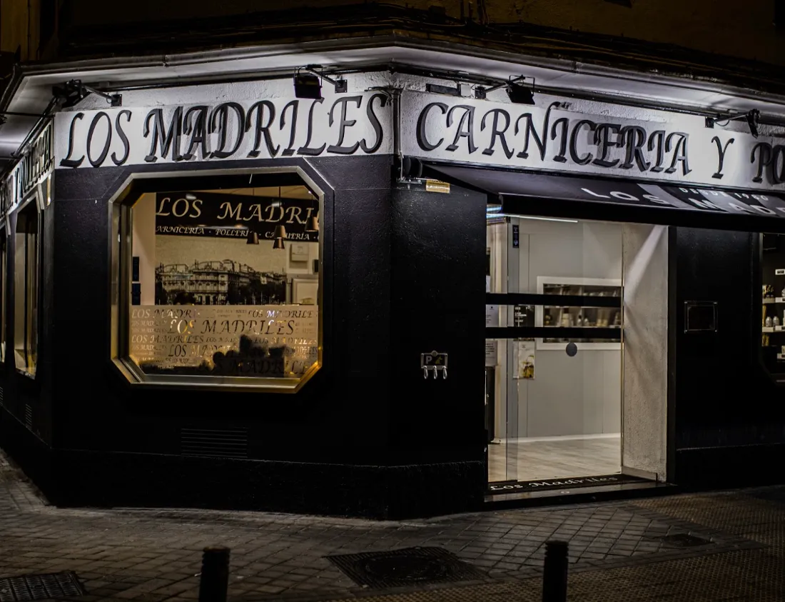 Fachada negra de Carnicería Los Madriles con el rótulo iluminado